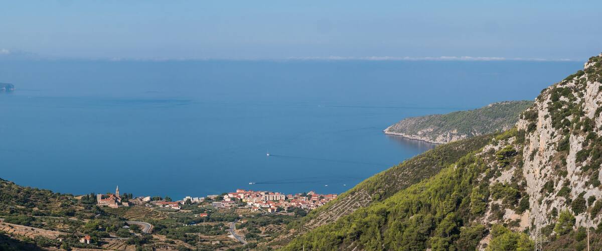 A coastal town nestled between hills, with a clear view of the sea and a distant island.