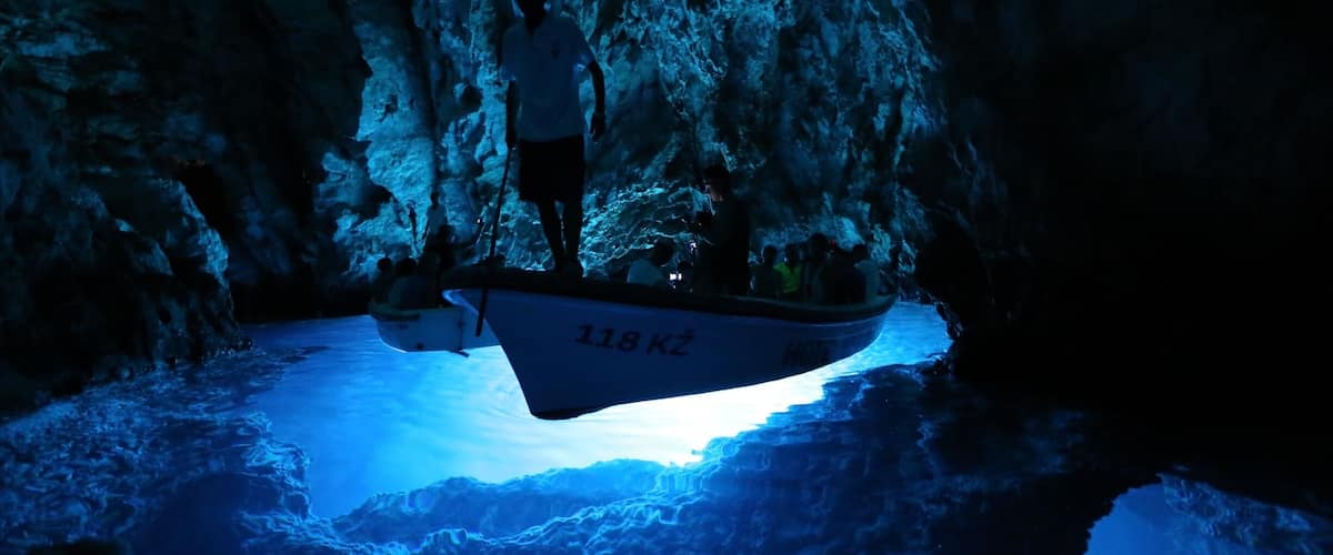 A boat labeled '118 KZ' in a cave with a blue light illuminating the water.