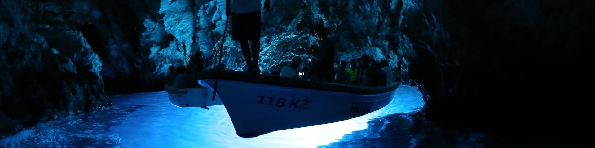 A boat labeled '118 KZ' in a cave with a blue light illuminating the water.