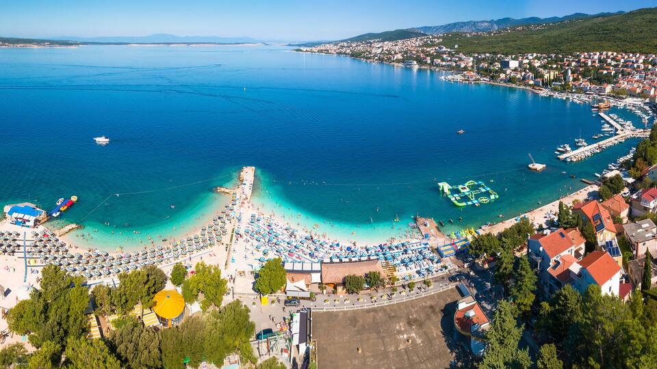 A coastal town with a beach, clear blue waters, and a marina.