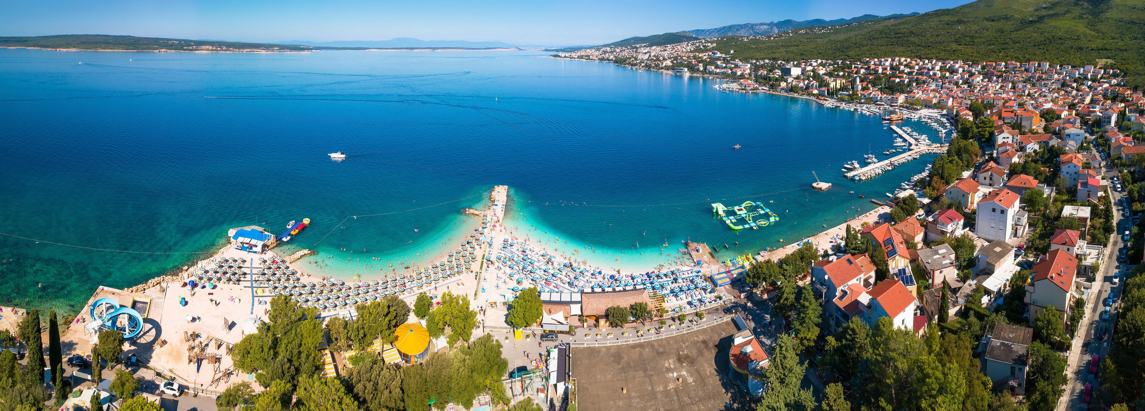 A coastal town with a beach, clear blue waters, and a marina.