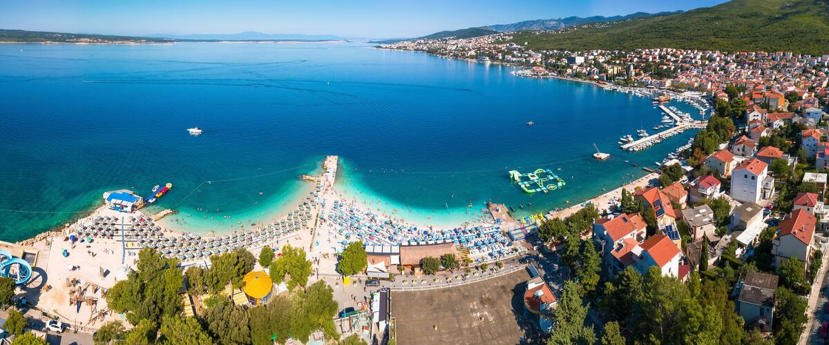 A coastal town with a beach, clear blue waters, and a marina.