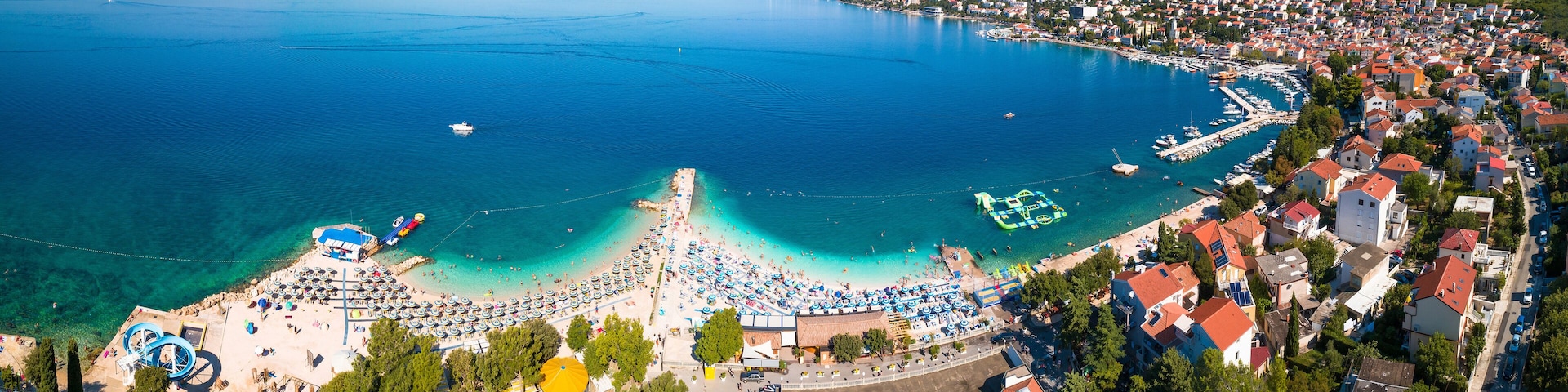 A coastal town with a beach, clear blue waters, and a marina.