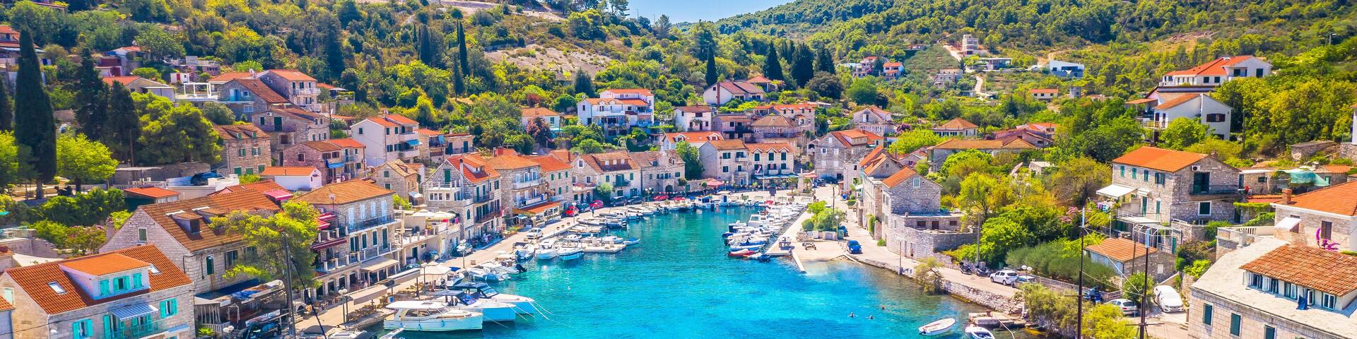 Aerial view of the tranquil bay in Stomorska on Solta Island, Croatia, featuring crystal-clear turquoise Adriatic waters, traditional seaside houses, and lush greenery in a peaceful setting