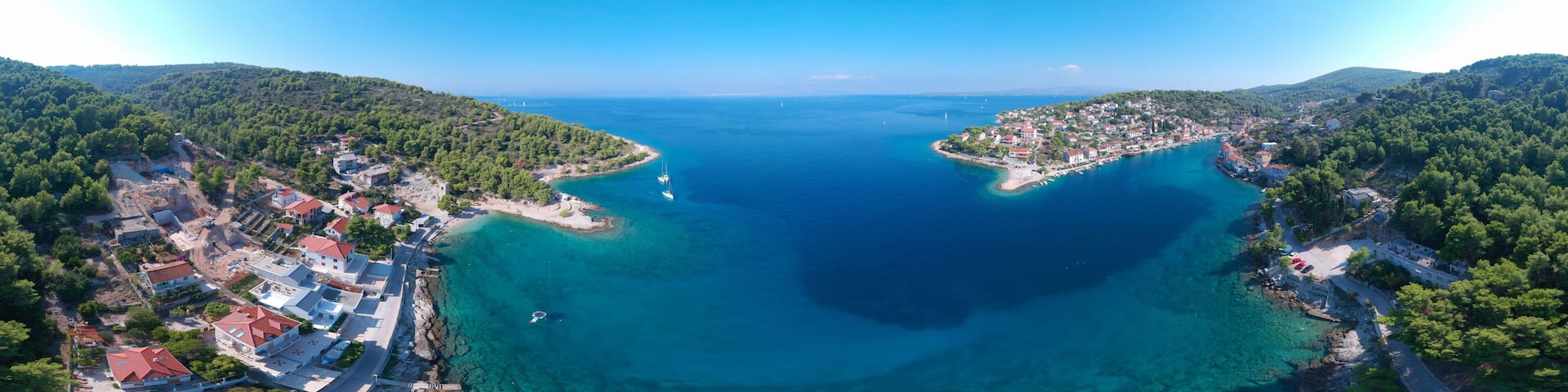A coastal town with clear blue waters, surrounded by lush green hills.