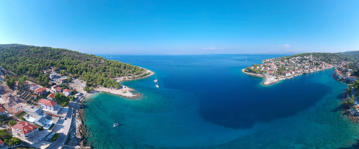 A coastal town with clear blue waters, surrounded by lush green hills.