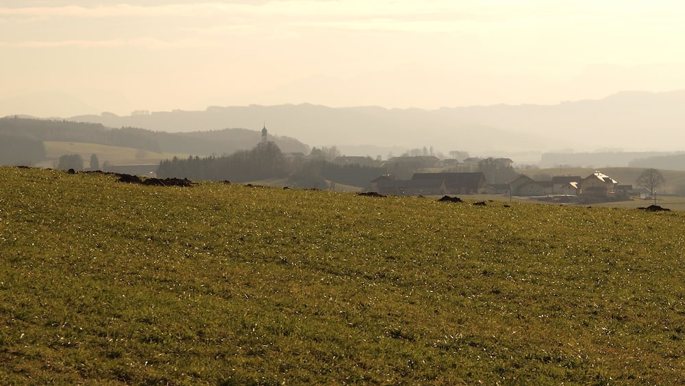 A misty rural landscape with rolling hills, scattered houses, and a prominent church tower.