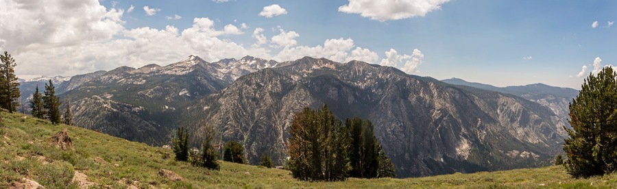 A mountain range with snow-capped peaks, a clear sky, and scattered clouds.