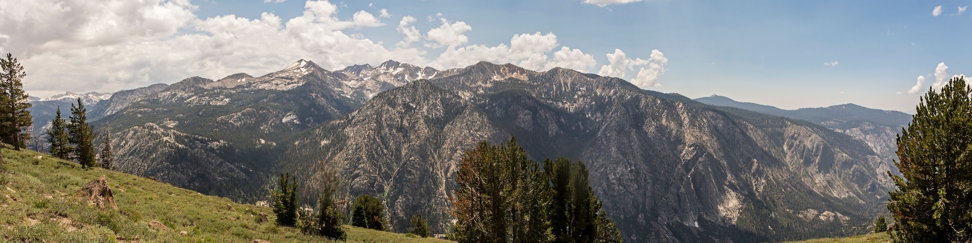 A mountain range with snow-capped peaks, a clear sky, and scattered clouds.