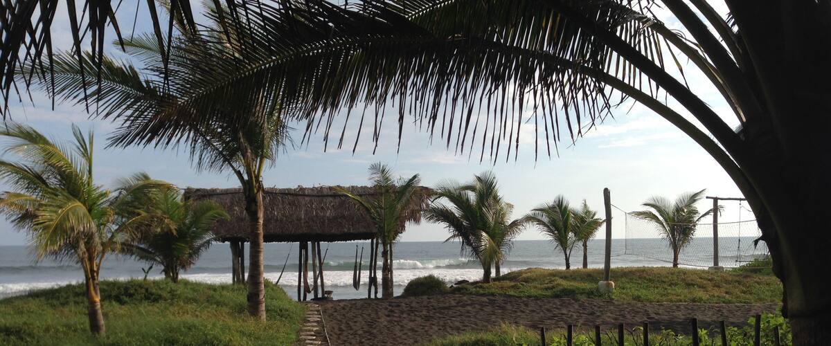 A beach path leading to a thatched structure with palm trees and the ocean in the background.
