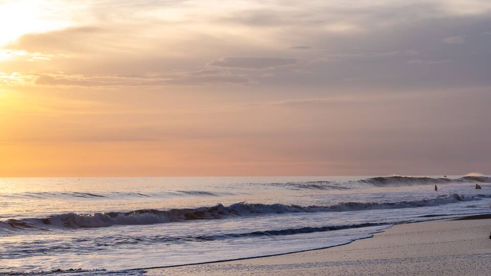 A beach with waves and a sunset.