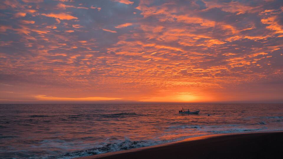A sunset over the ocean with a boat on the water.