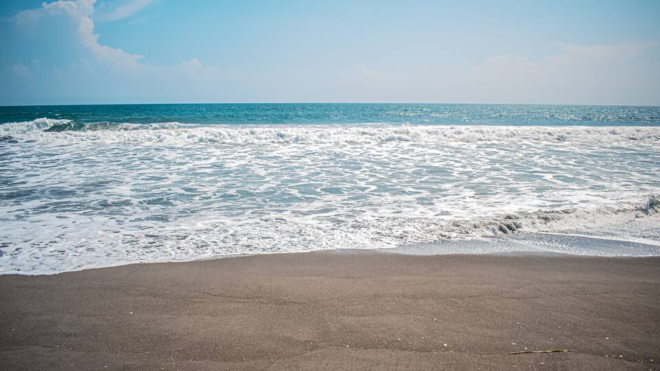 A beach with waves crashing onto the shore under a clear sky.
