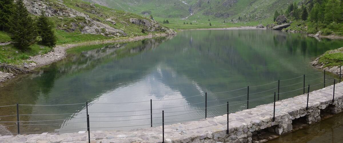A serene mountain lake with a stone bridge and a small cabin in the valley.