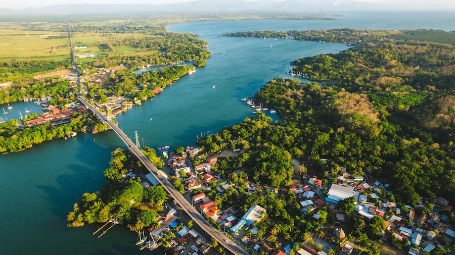 Vista aérea de un pueblo costero con un puente, abundante vegetación y una gran masa de agua.