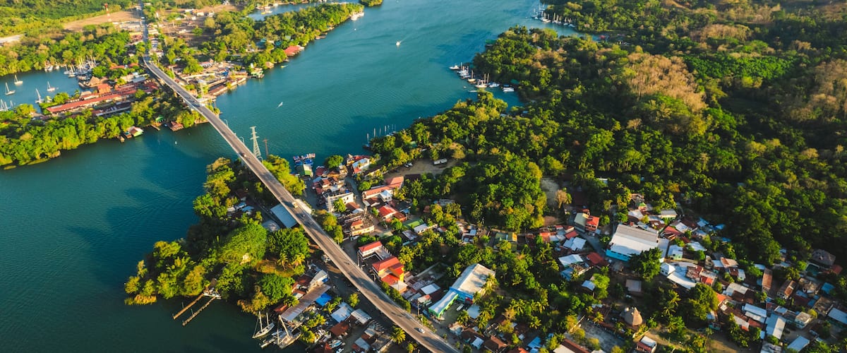 An aerial view of a coastal town with a bridge, dense greenery, and a large body of water.