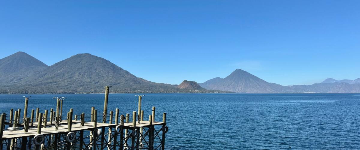 A wooden pier extending into a calm sea with mountains in the background.