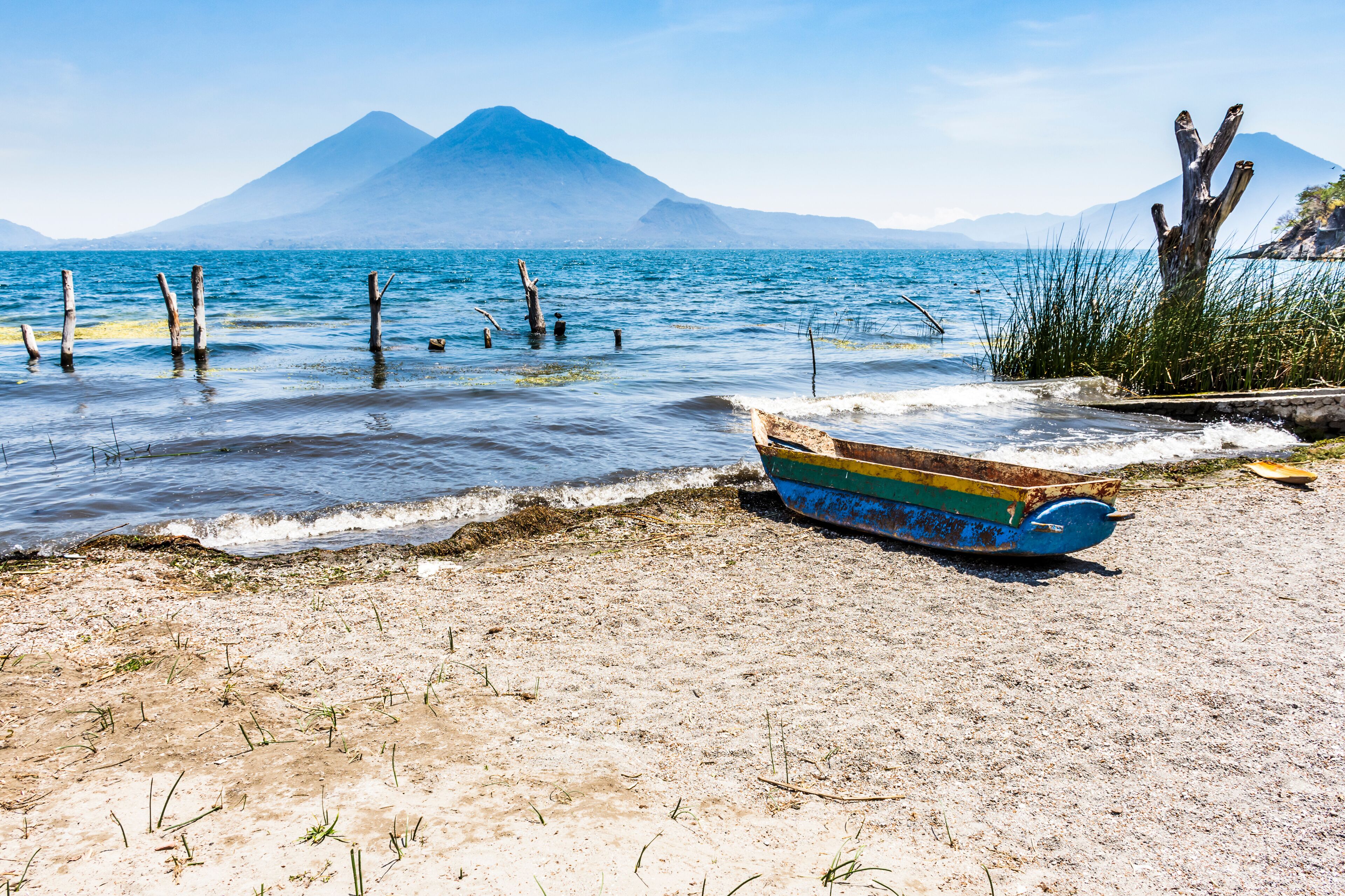 Traditional wooden boat on beach with Toliman & Atitlan volcanoes on horizon in lakeside town of Santa Catarina Palopo, Lake Atitlan, Guatemala.