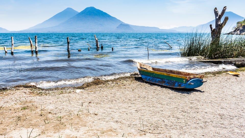 A beach with a colorful boat, a mountain in the background, and a clear sky.