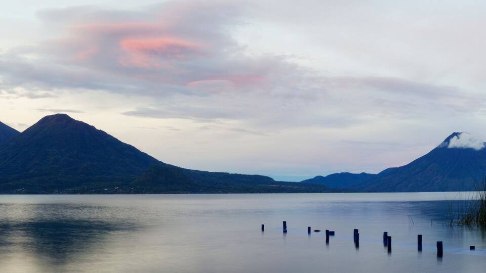 A calm lake with two prominent mountains in the background and a clear sky.