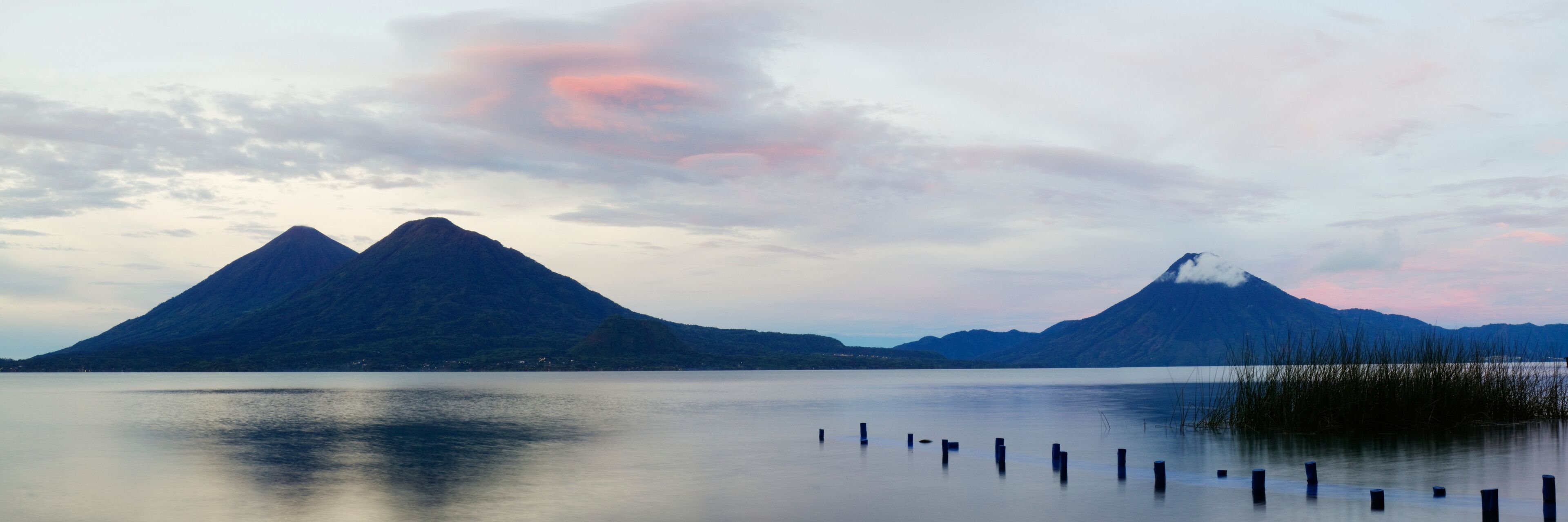 A calm lake with two prominent mountains in the background and a clear sky.