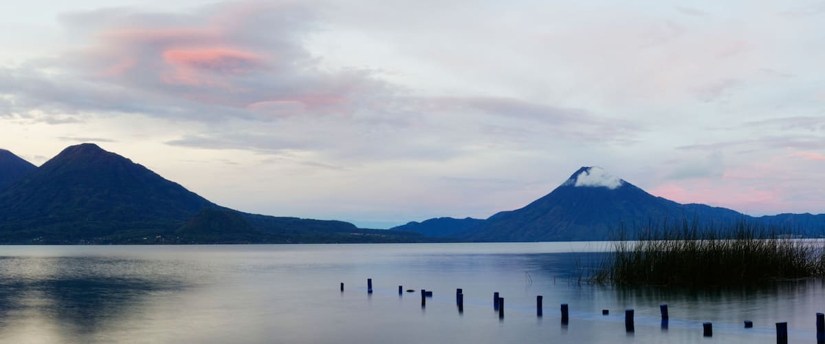A calm lake with two prominent mountains in the background and a clear sky.