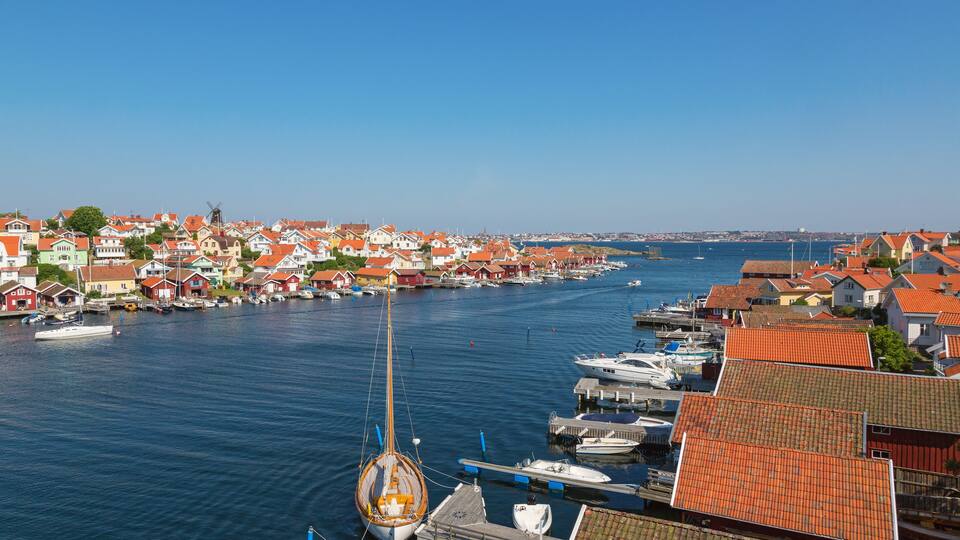 A coastal town with red-roofed houses, a windmill, and boats docked along the harbor.