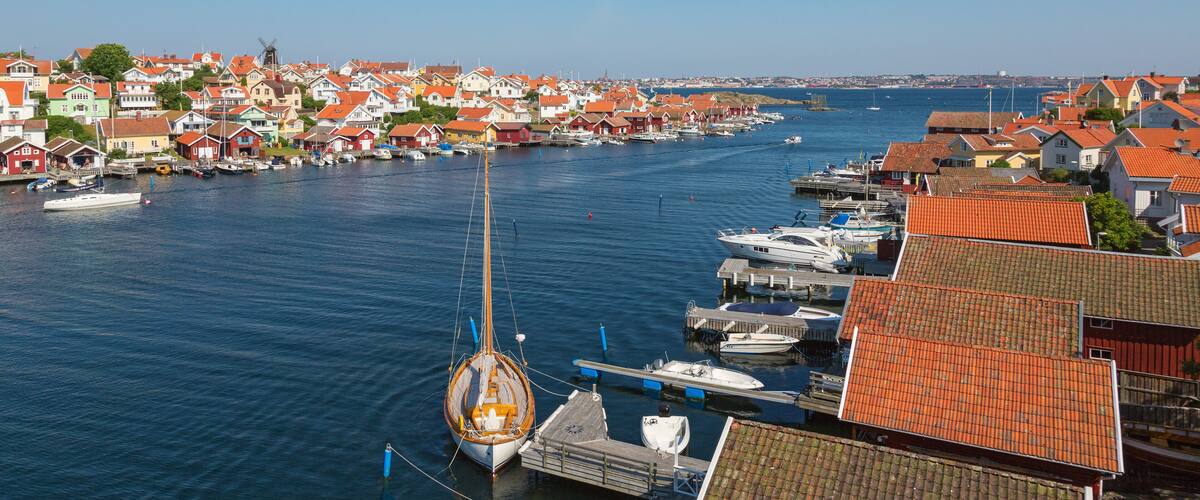 A coastal town with red-roofed houses, a windmill, and boats docked along the harbor.