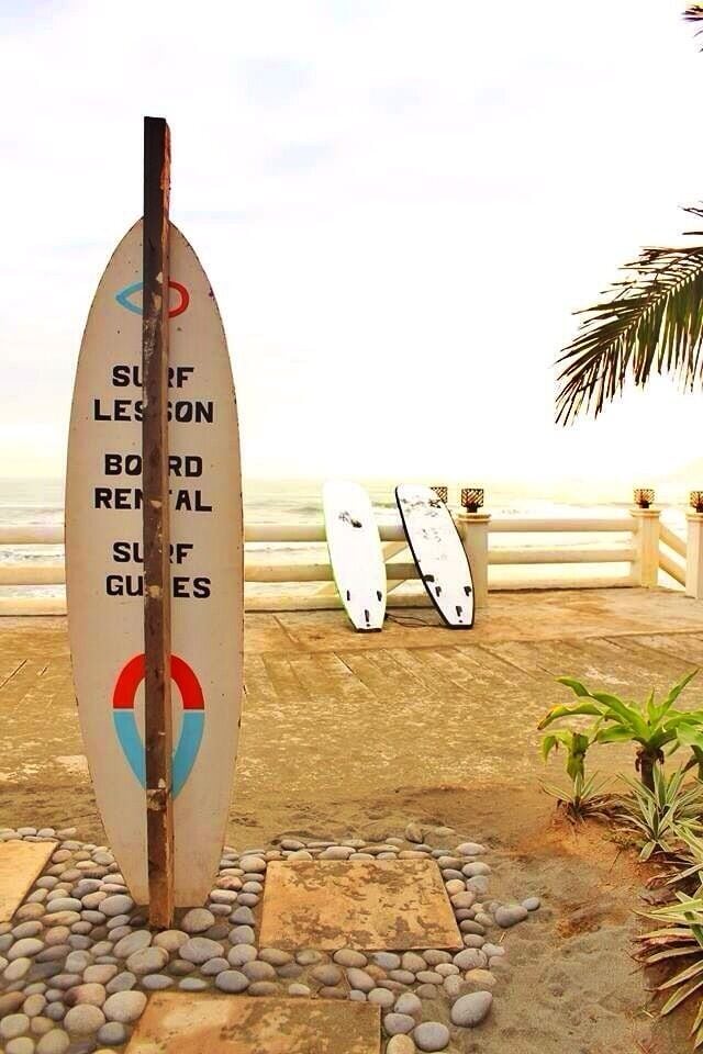 A surfboard rental sign with two surfboards leaning against a railing.
