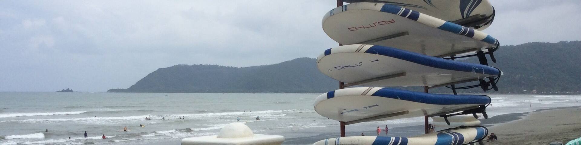 A stack of surfboards on a beach with waves and mountains in the background.