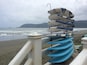 A stack of surfboards on a beach with waves and mountains in the background.