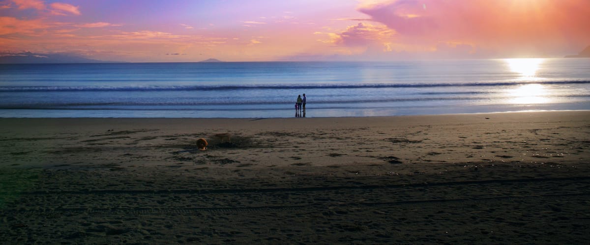 A beach with people standing near the water during sunset.