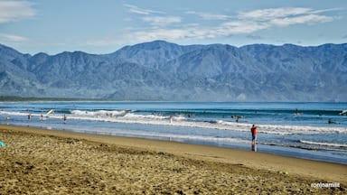 Una playa con olas, gente y montañas al fondo.