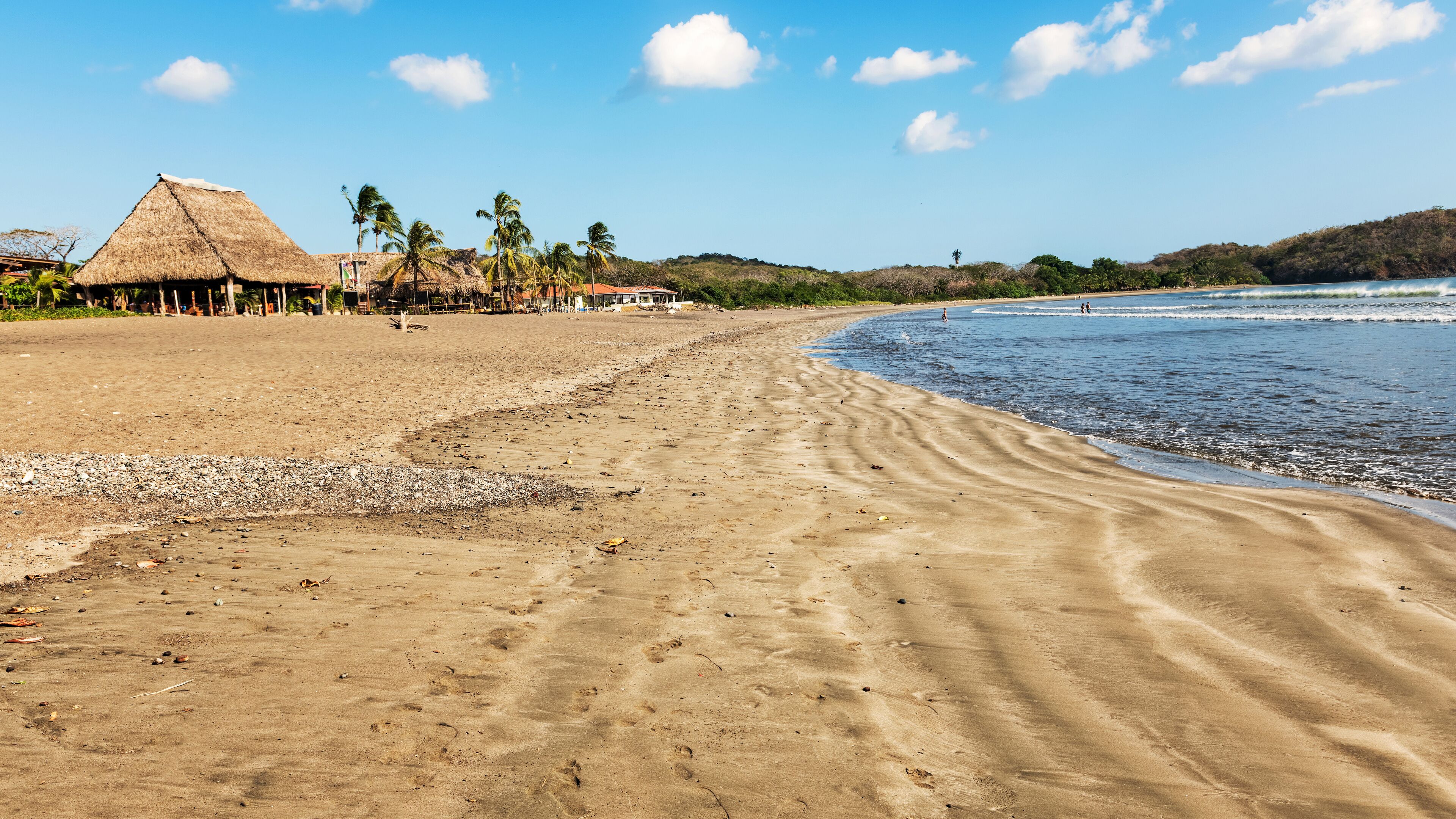 A sandy beach with footprints, palm trees, and thatched-roof huts.