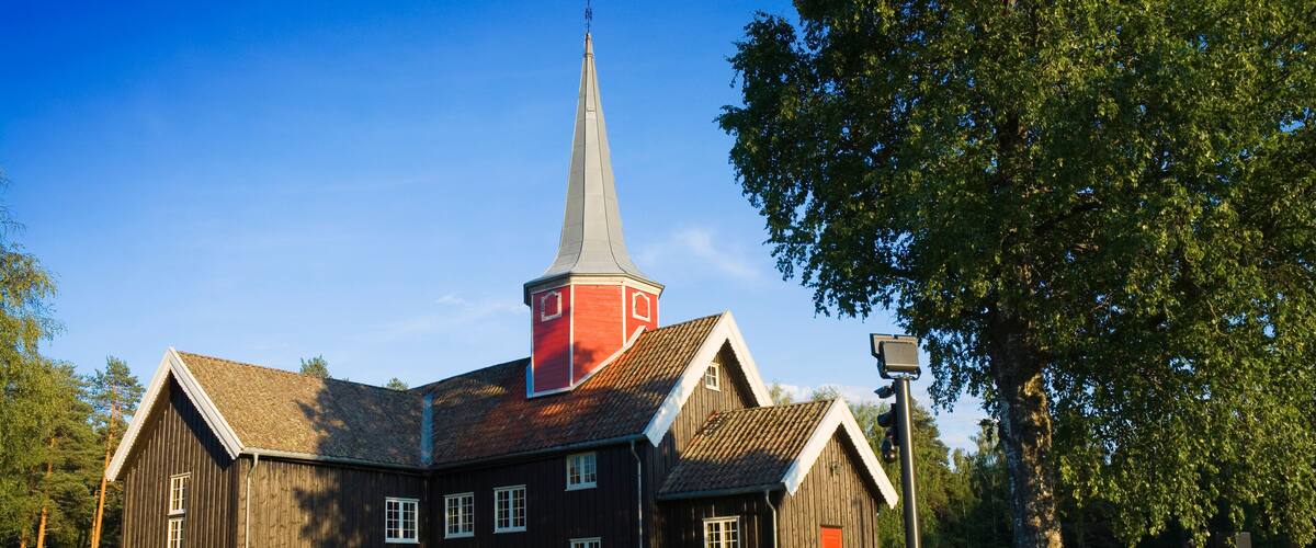 A wooden church with a red steeple and a stone wall in front.