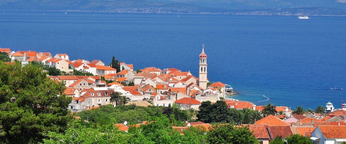 A coastal town with red-roofed buildings, a prominent clock tower, and a clear view of the sea.
