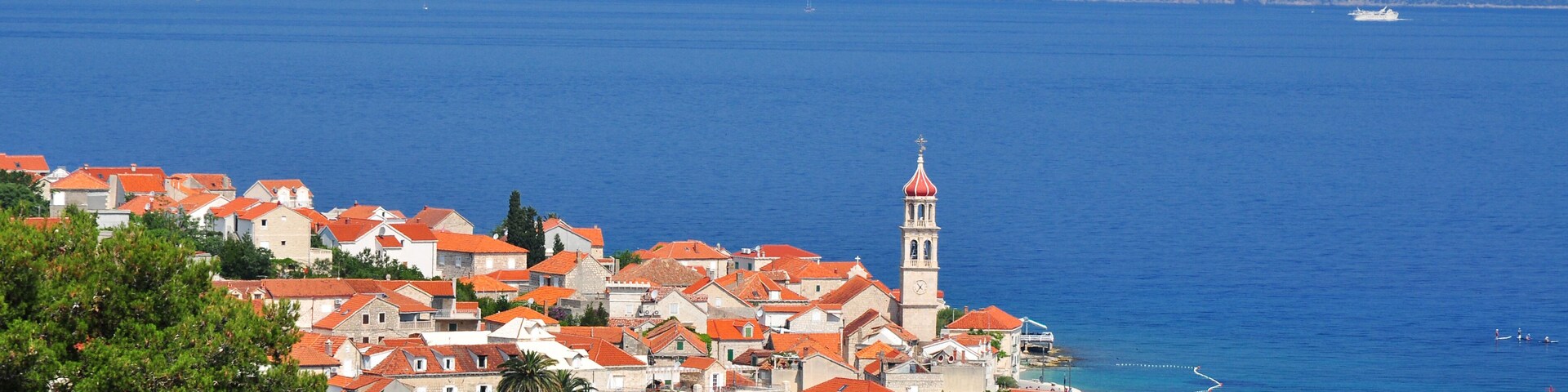 A coastal town with red-roofed buildings, a prominent clock tower, and a clear view of the sea.