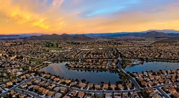 A residential area with a central lake surrounded by houses, roads, and distant mountains.