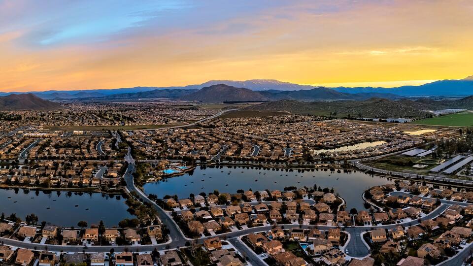A residential area with a central lake surrounded by houses, roads, and distant mountains.