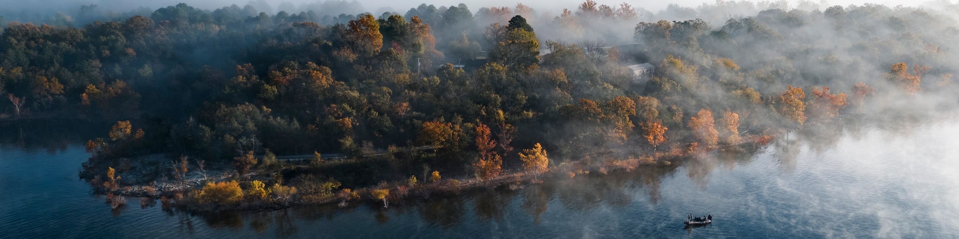 A misty forested island surrounded by calm water, with a boat in the distance.
