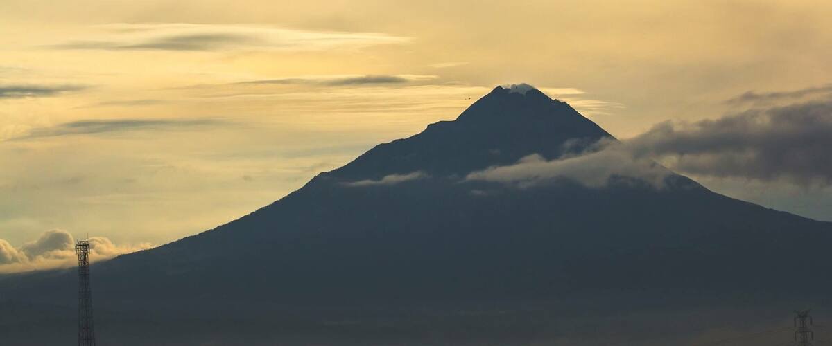 A mountain with a peak, surrounded by clouds and a power line tower.