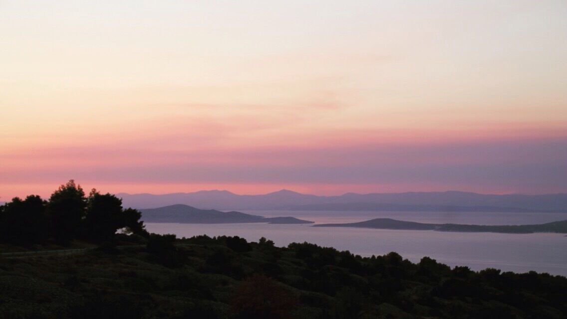 A coastal landscape with a calm sea, distant mountains, and a forested foreground.