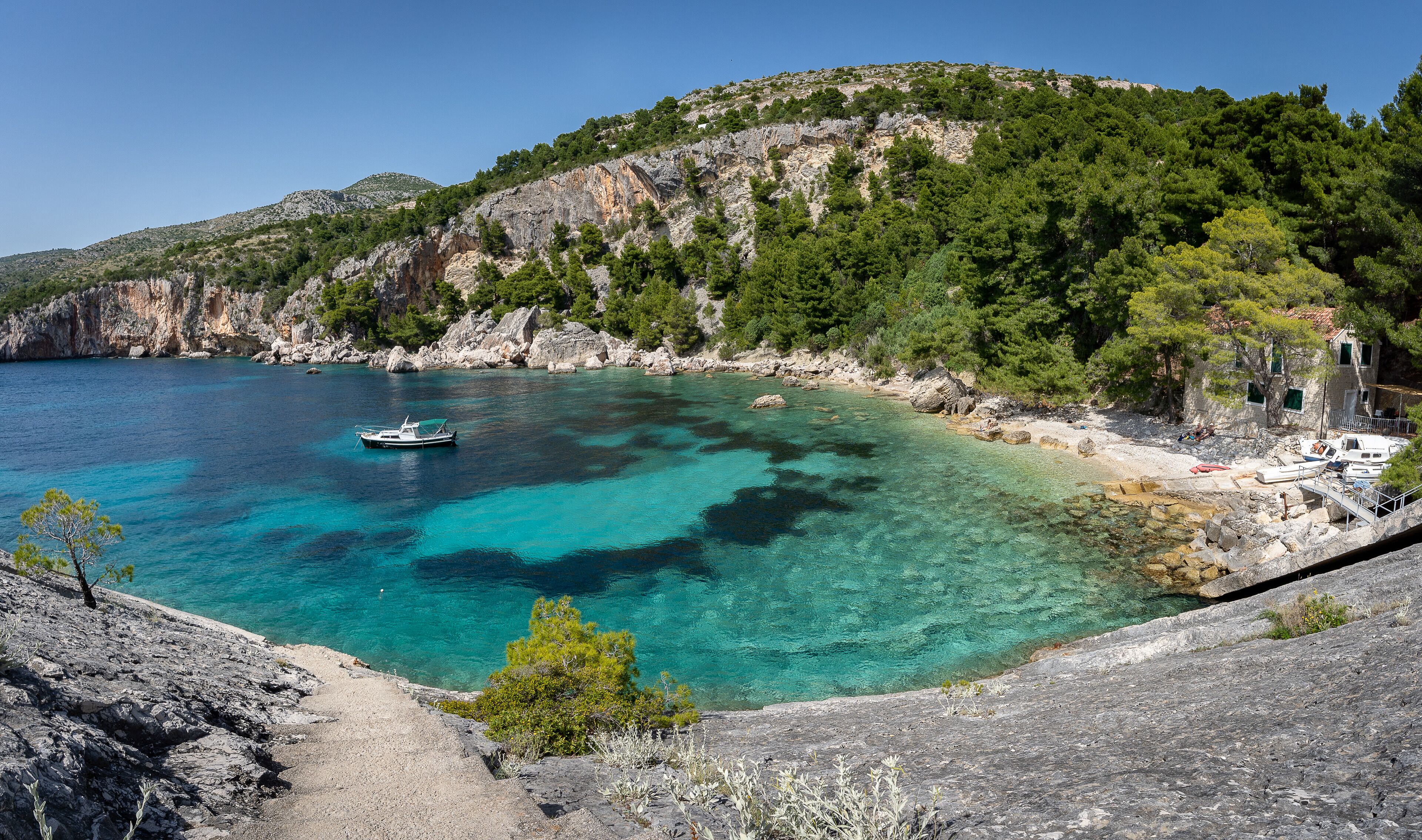 A coastal landscape with clear turquoise waters, rocky cliffs, and a boat anchored near the shore.