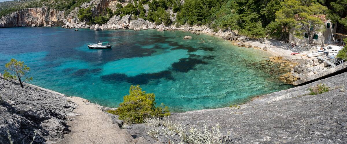 A coastal landscape with clear turquoise waters, rocky cliffs, and a boat anchored near the shore.