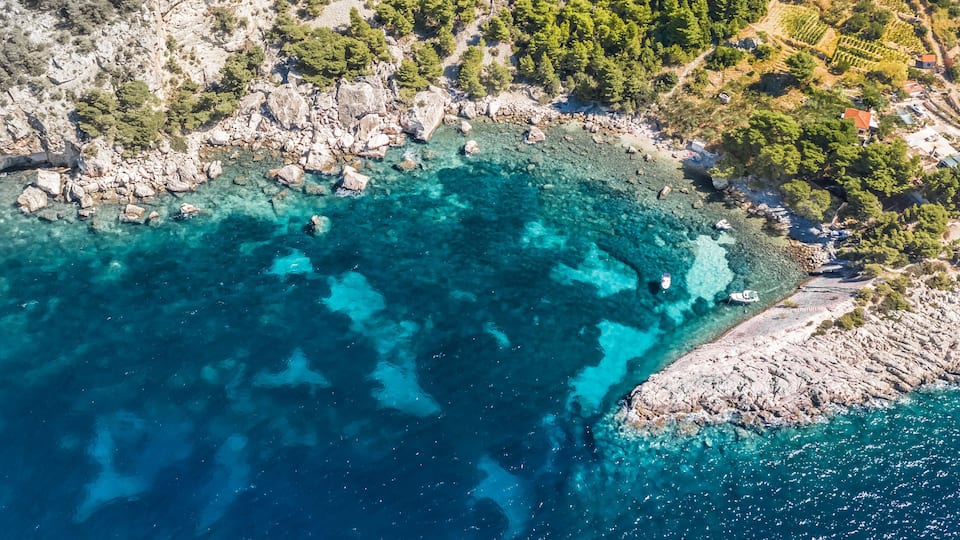 A coastal landscape with clear turquoise waters, rocky shores, and scattered buildings.