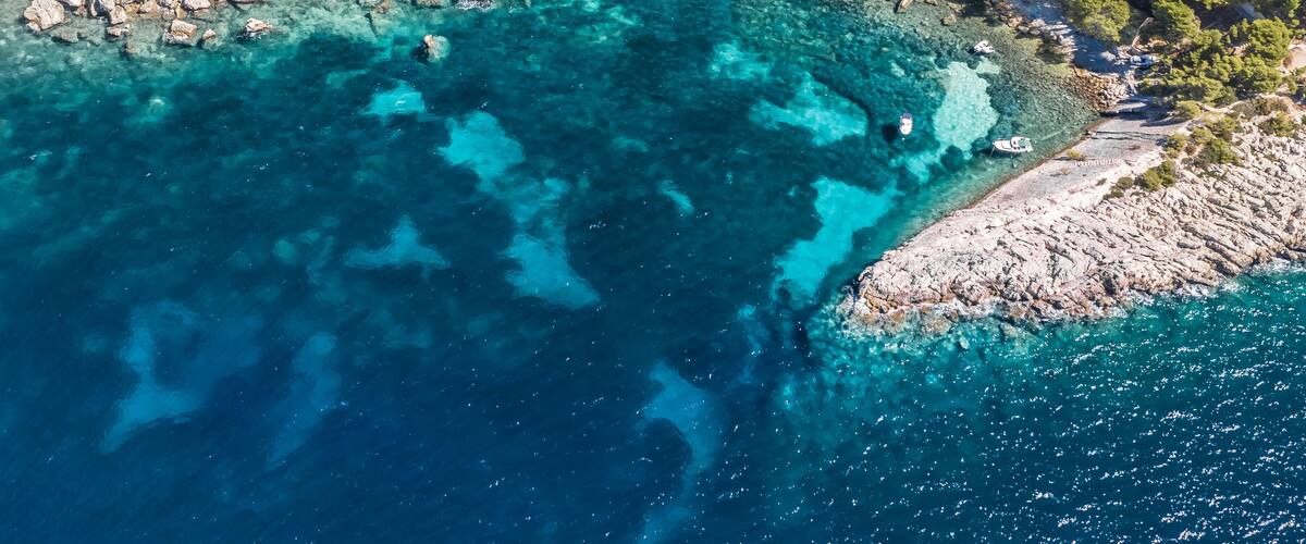 A coastal landscape with clear turquoise waters, rocky shores, and scattered buildings.