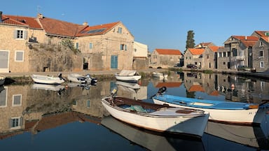 A calm harbor with boats docked, stone buildings with red roofs, and a clear blue sky.