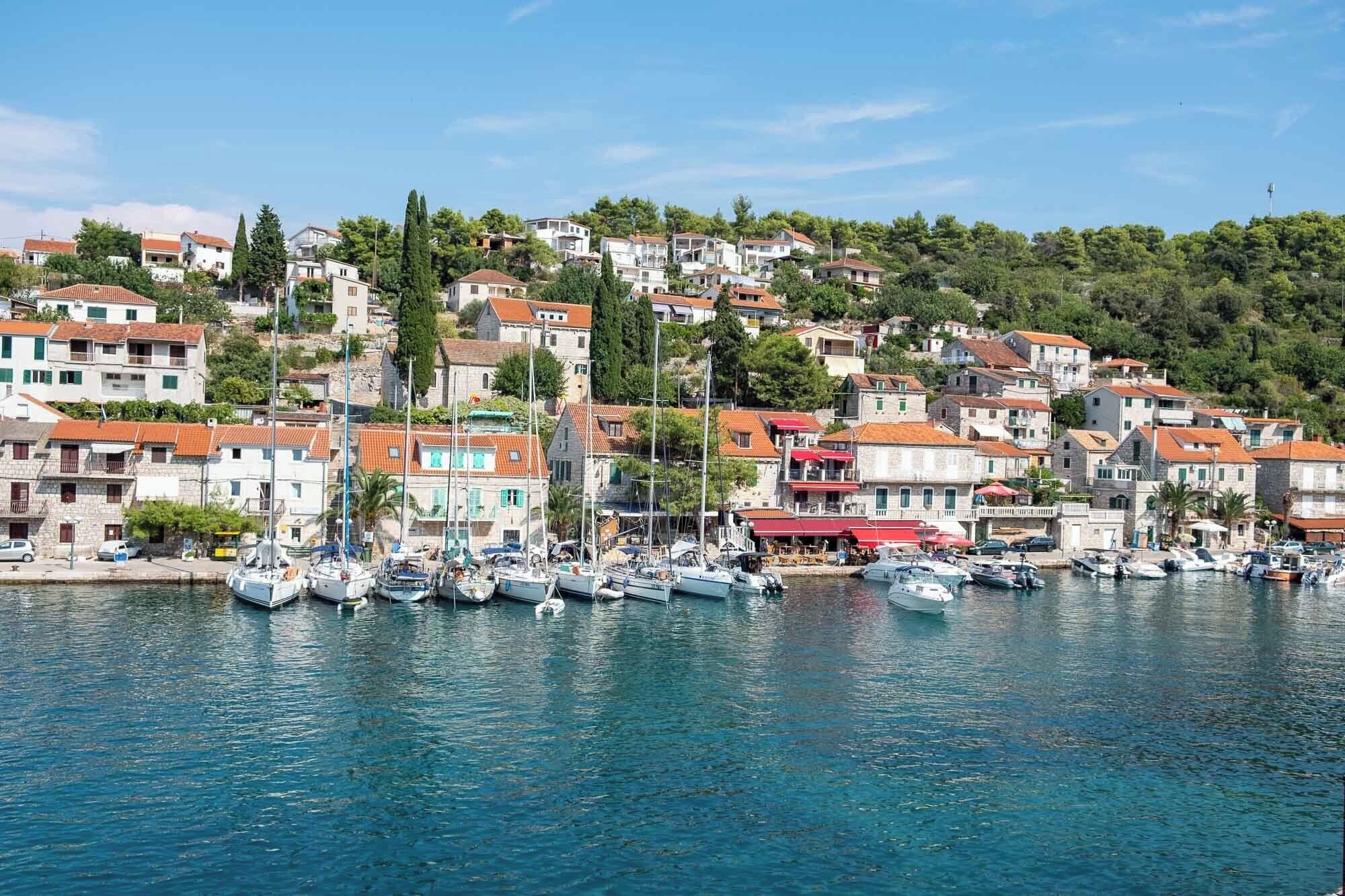 A coastal town with a marina filled with boats, surrounded by terraced houses and lush greenery.