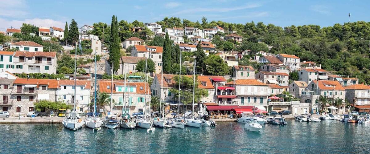 A coastal town with a marina filled with boats, surrounded by terraced houses and lush greenery.