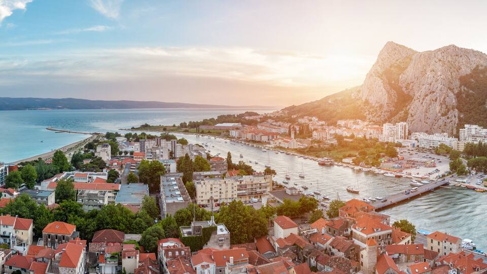 A coastal town with red-roofed buildings, a marina, and rocky cliffs.